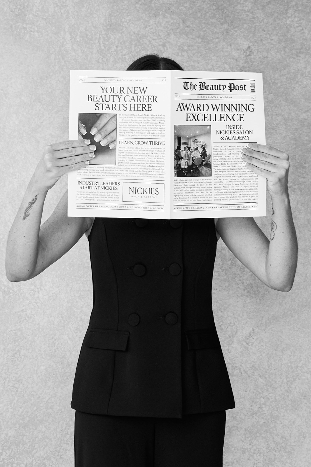 A black and white portrait of Nickie behind her newspaper