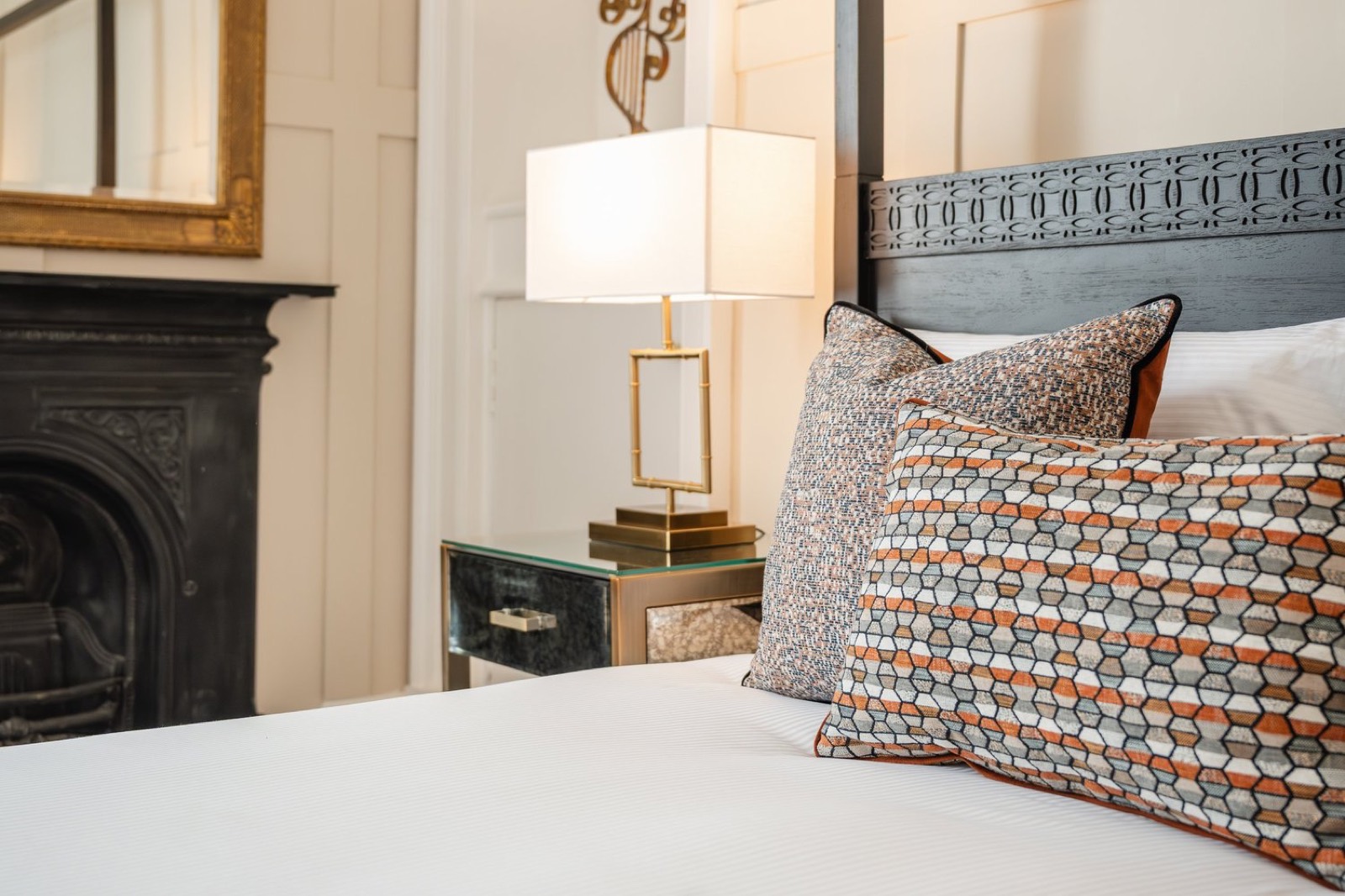 A bedroom with a cast iron fireplace and patterned cushions