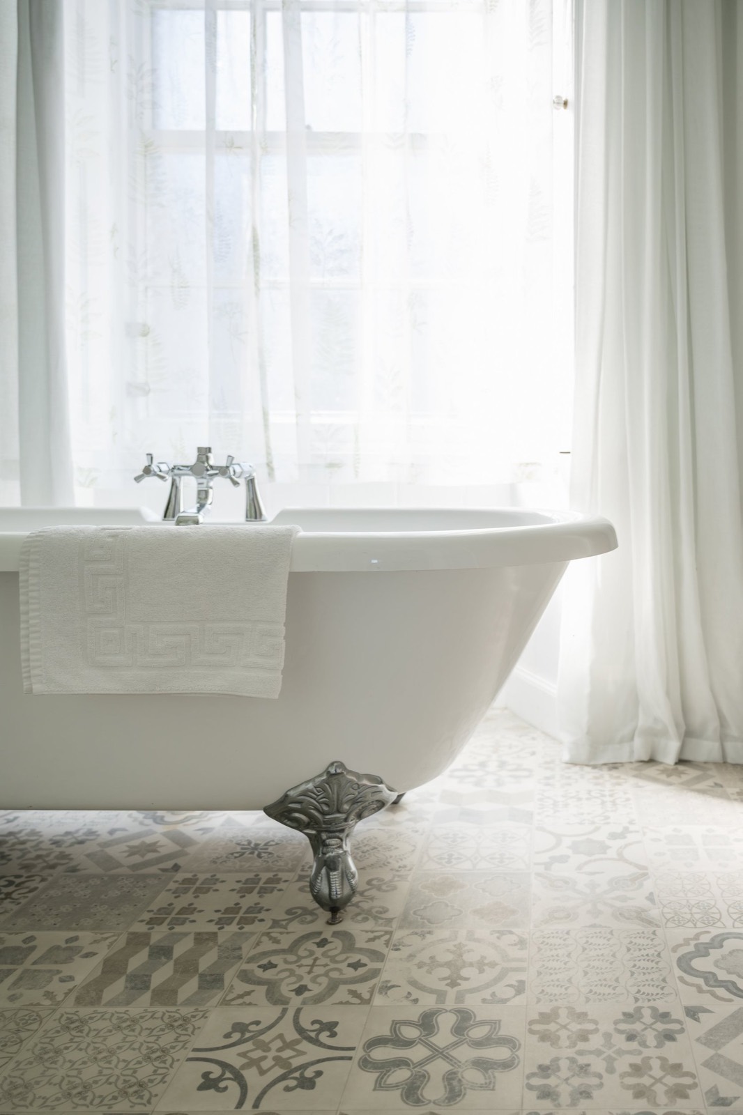 A roll-top bath on patterned tiles by a window