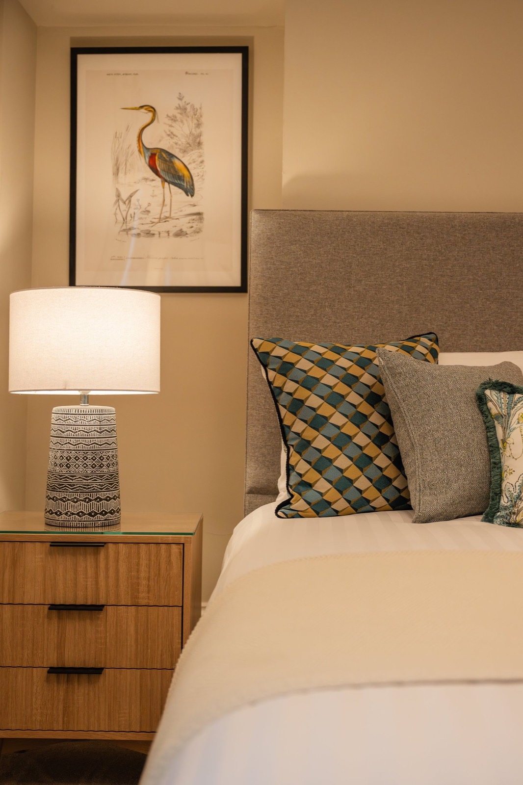 A bedside with a heron print and lamp