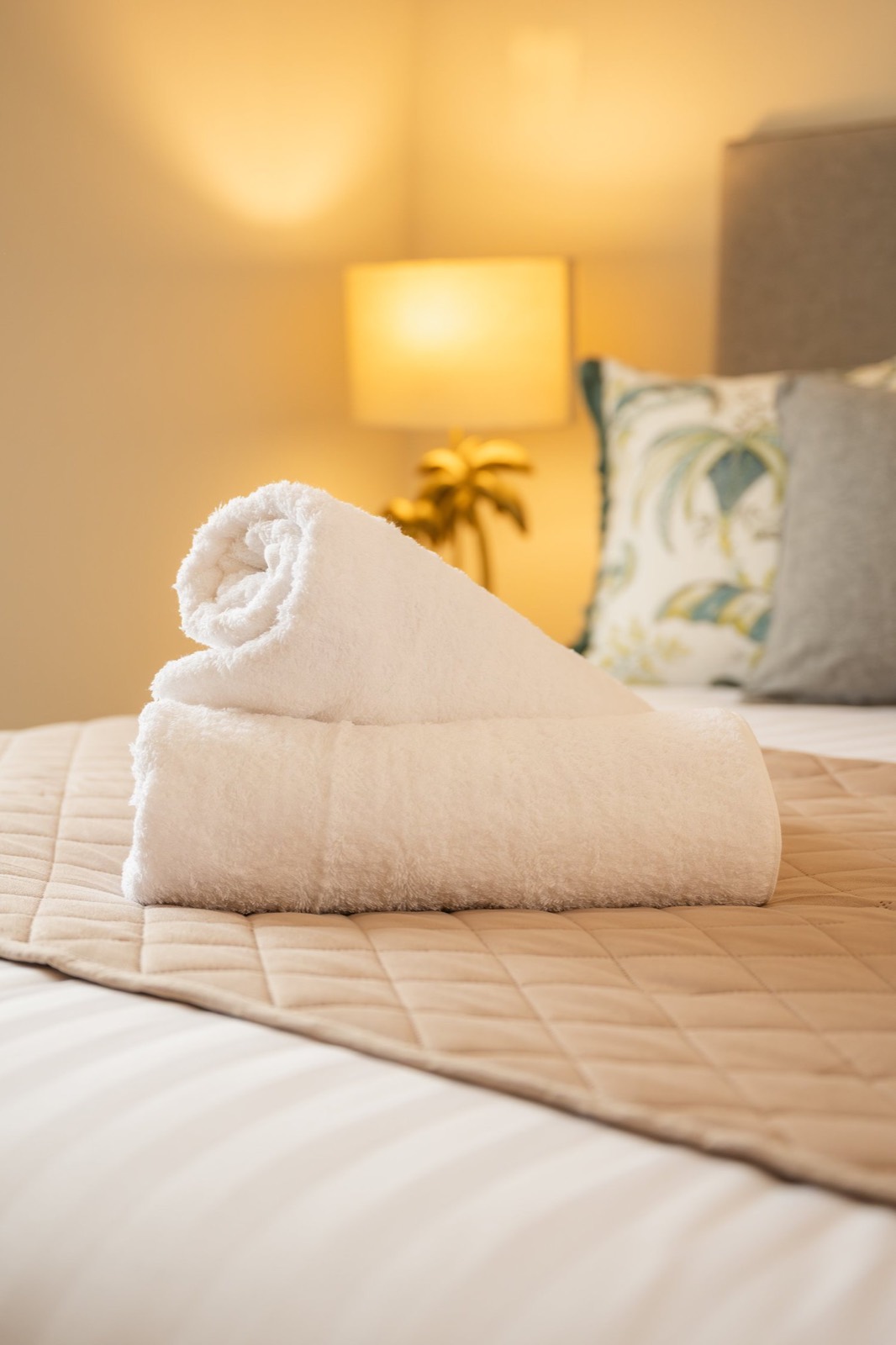 Rolled towels on a made bed in lamplight