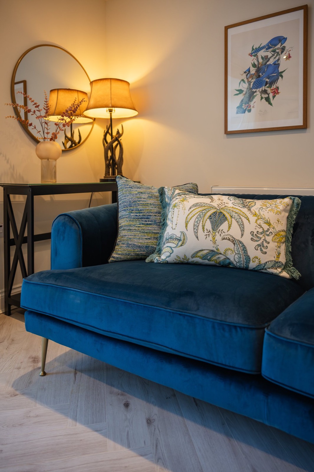 A blue velvet sofa beneath a bird print