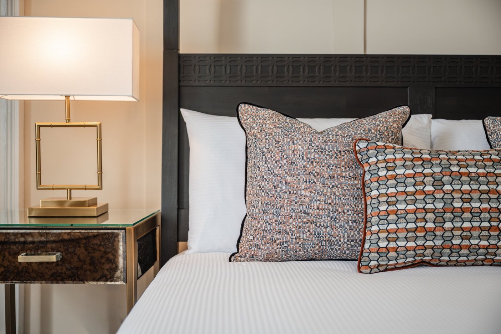 A bedside lamp and patterned cushions on a dark headboard