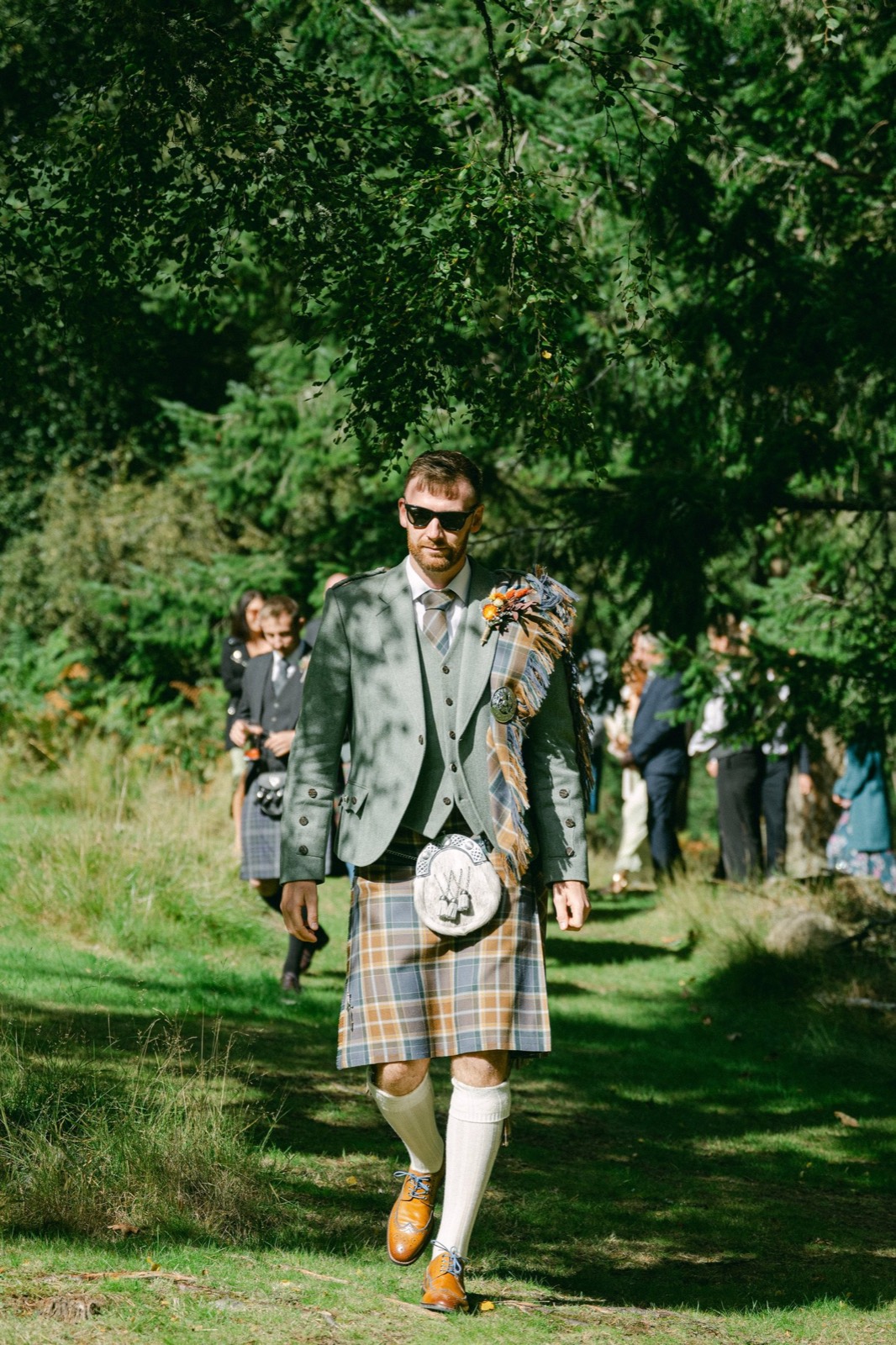 A groom in a kilt walking through the trees
