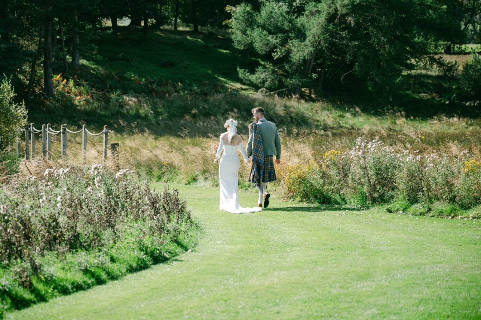 A bride and groom walking through a meadow