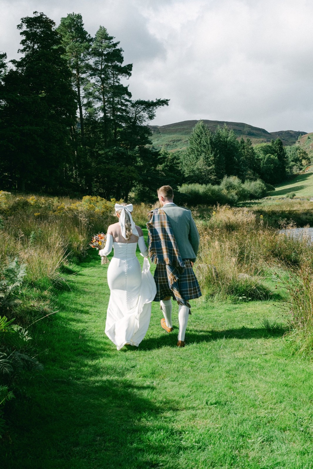 A bride and groom walking away through long grass