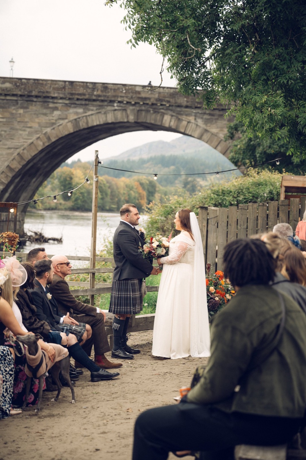 A riverside ceremony beneath a stone bridge