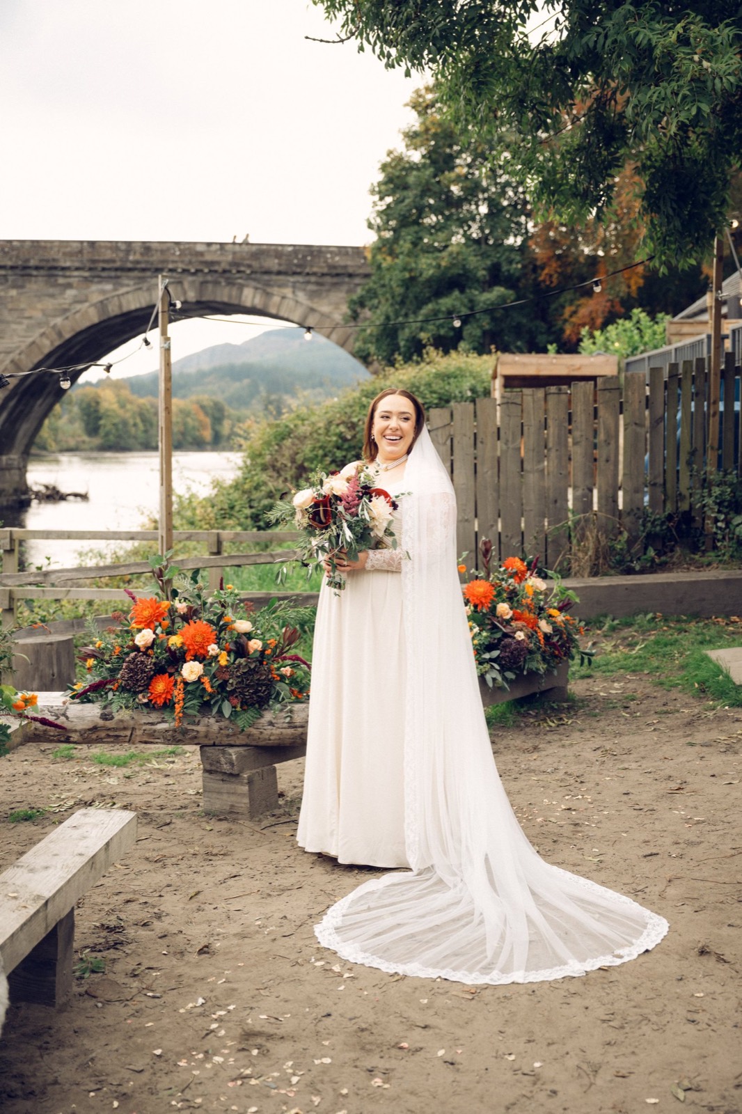 A bride with a long veil by a stone bridge