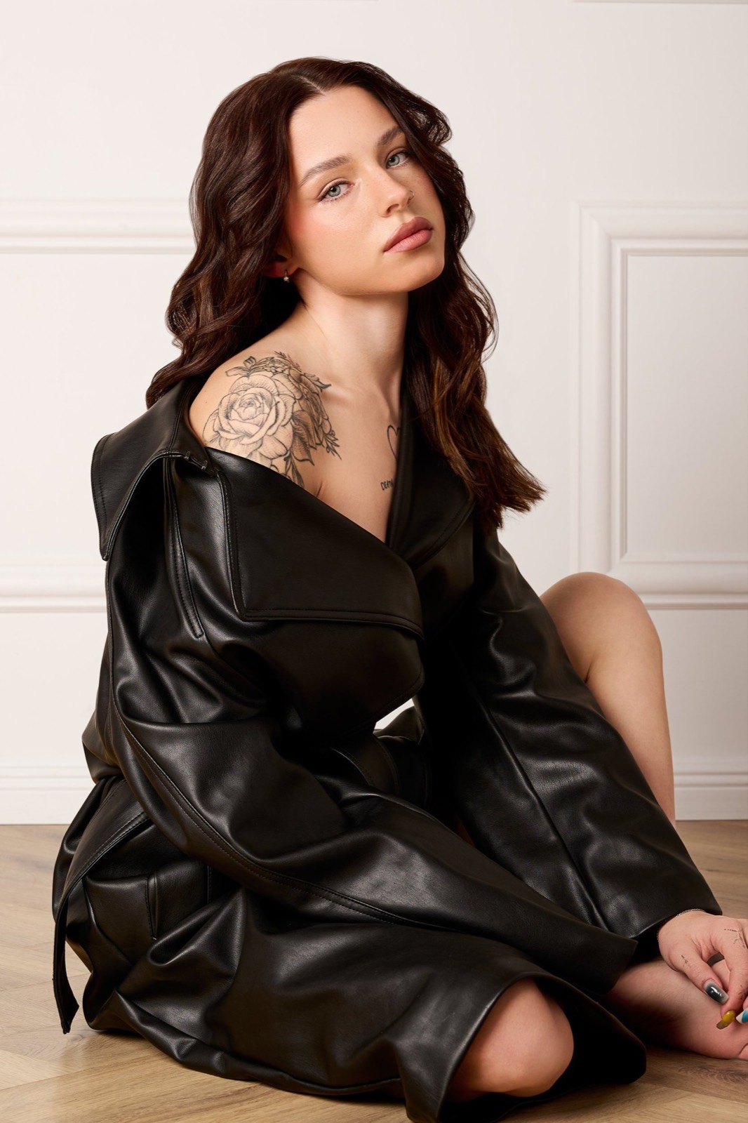 A woman in a black leather coat seated on the studio floor