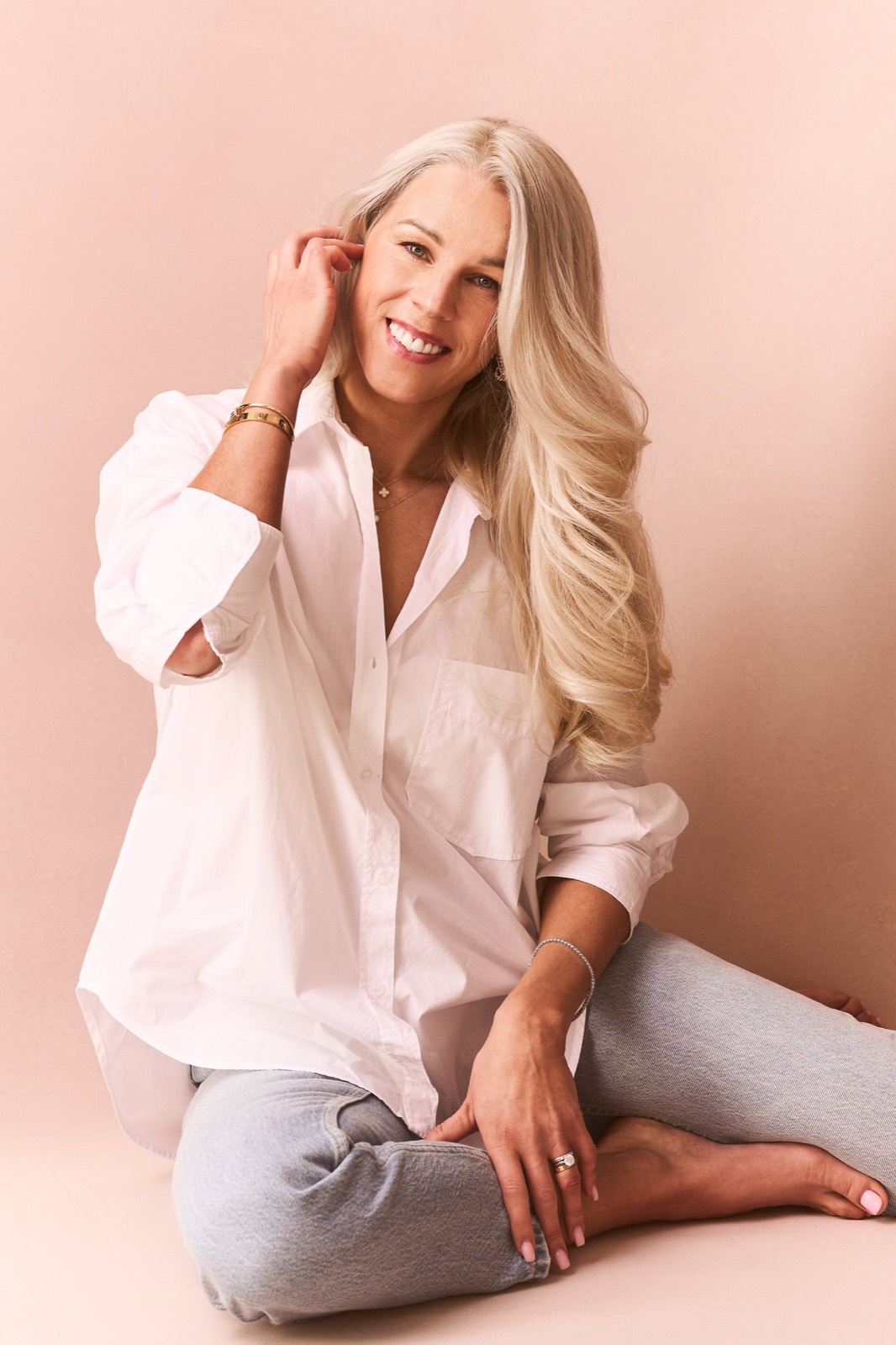 A smiling woman in a white shirt against a blush backdrop