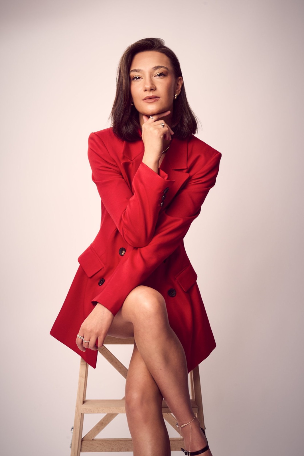 A woman in a red blazer seated against blush