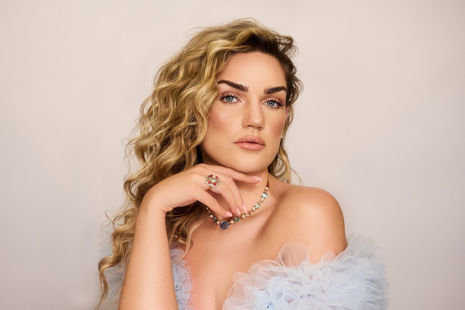 A woman with golden curls in soft blush light, resting her chin on her hand